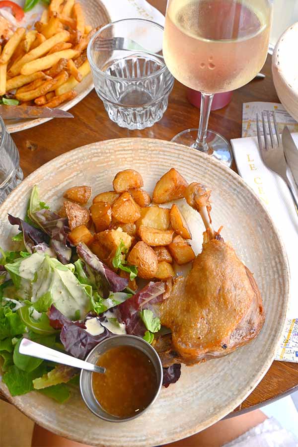 crispy-duck-confit-served-with-roasted-potatoes-salad-and-white-wine-at-a-paris-bistro