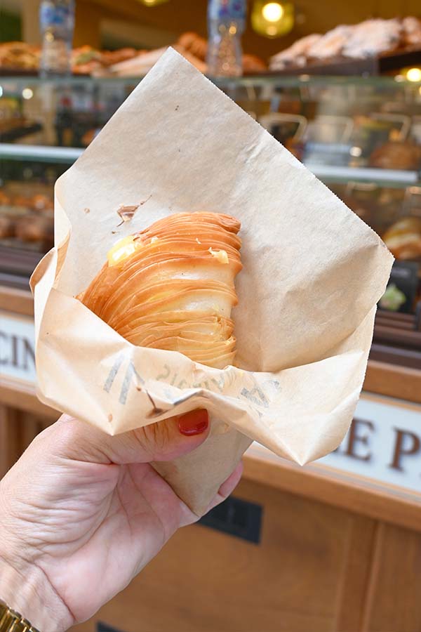 flaky-sfogliatella-or-lobster-tail-pastry-held-in-a-paper-wrapper-outside-a-bakery