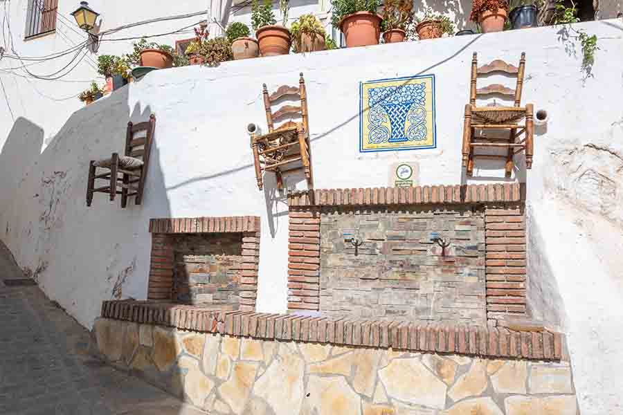 stone-fountain-wooden-chairs-mounted-wall-Almachar-Spain-white-villages-Andalusia